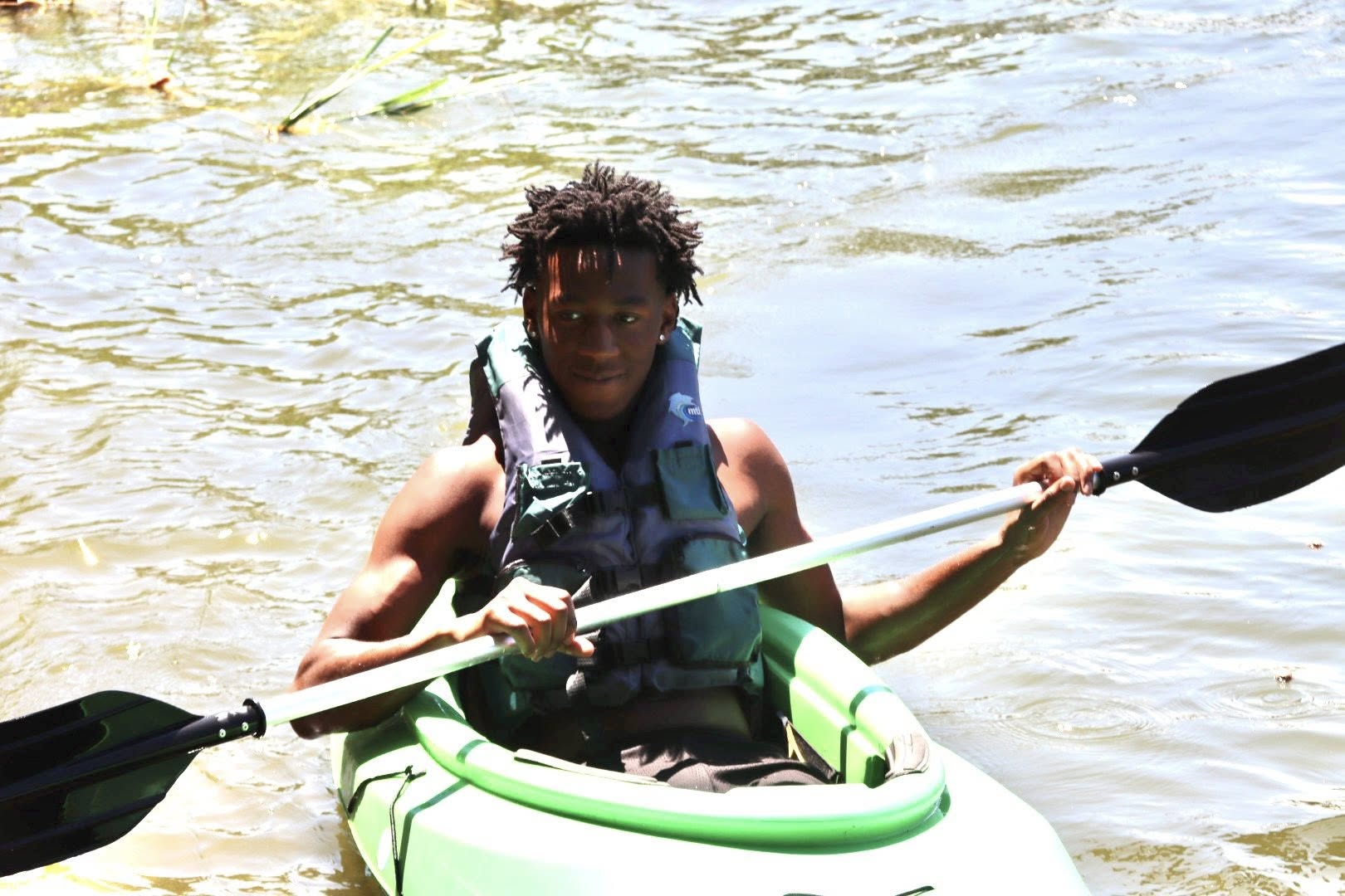  A teenage boy kayaking in a lake.